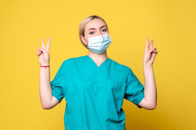 노란색 벽에 의료 셔츠와 마스크에 젊은 여성 의사의 전면보기