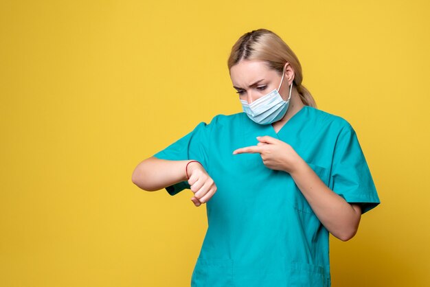 노란색 벽에 그녀의 손목에 의료 셔츠와 멸균 마스크 lookign 젊은 여성 의사의 전면보기