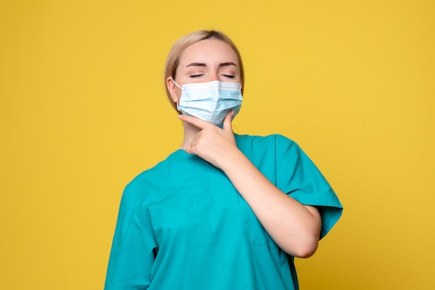 黄色の壁で考える医療シャツと滅菌マスクの若い女性医師の正面図