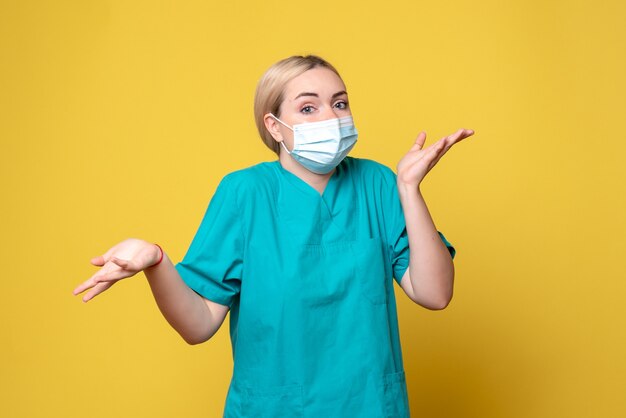 Вид спереди молодой женщины-врача в медицинской рубашке и стерильной маске на желтой стене