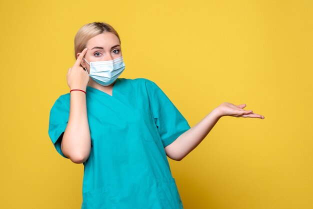 노란색 벽에 의료 셔츠와 멸균 마스크에 젊은 여성 의사의 전면보기