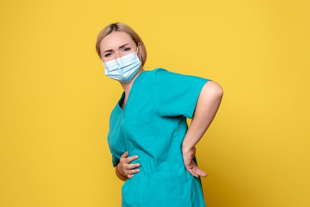 Front view of young female doctor in medical shirt and sterile mask on yellow wall