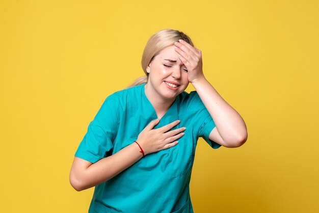 Front view of young female doctor in medical shirt suffering from headache on yellow wall
