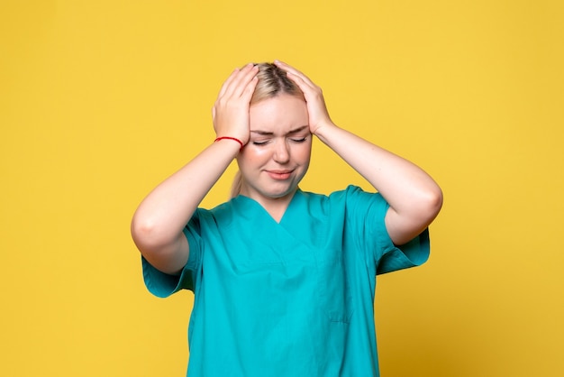 Front view of young female doctor in medical shirt suffering from headache on yellow wall