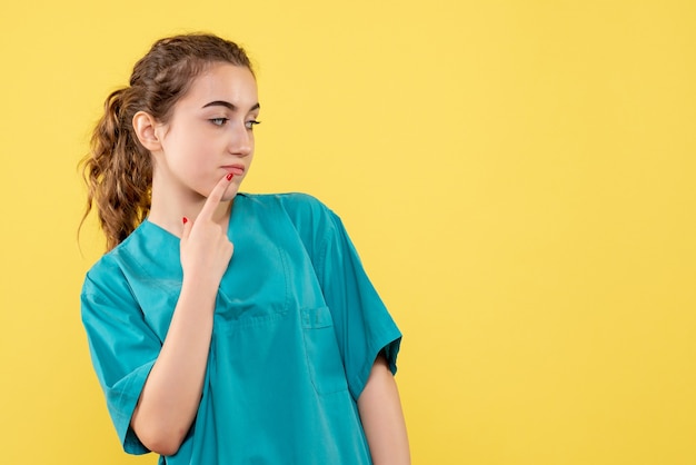 黄色の壁で考える医療シャツの若い女性医師の正面図