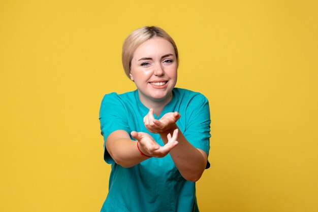Front view of young female doctor in medical shirt with hurt arm on yellow wall