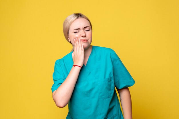 Front view of young female doctor in medical shirt with toothache on yellow wall