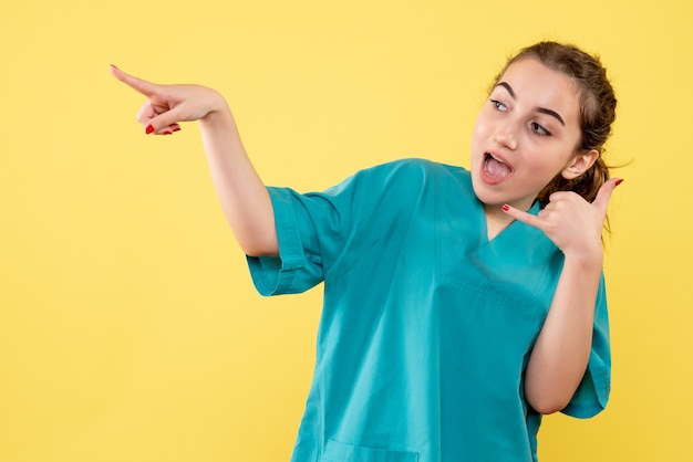 Vista frontale del giovane medico femminile in camicia medica sulla parete gialla