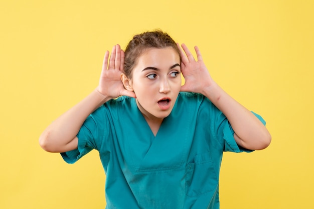 Front view of young female doctor in medical shirt on yellow wall