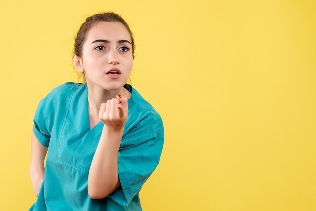 Front view of young female doctor in medical shirt on yellow wall