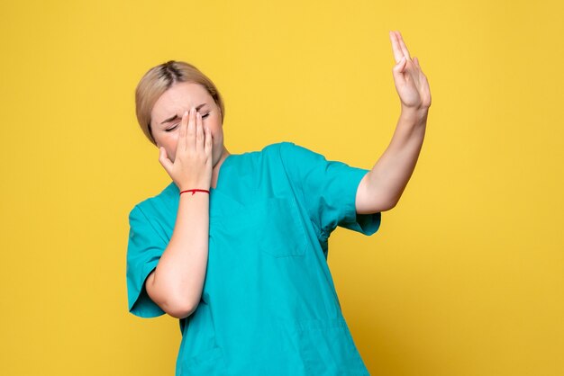 Front view of young female doctor in medical shirt on yellow wall