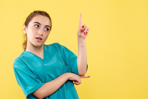 Front view of young female doctor in medical shirt on yellow wall