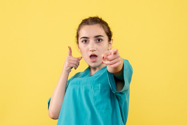 Front view of young female doctor in medical shirt on yellow wall