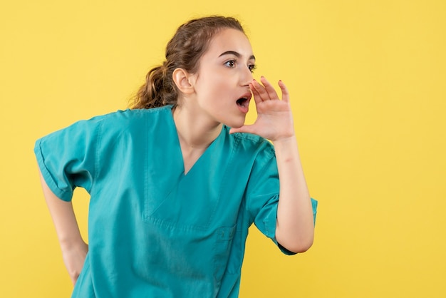 Front view of young female doctor in medical suit calling someone on yellow wall