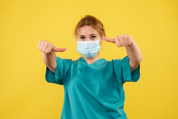 Front view of young female doctor in medical suit and mask on yellow wall