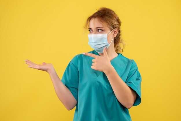 Front view of young female doctor in medical suit and mask on yellow wall