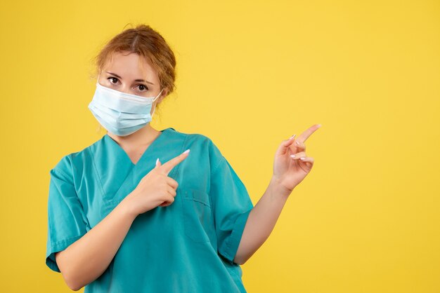 Front view of young female doctor in medical suit and mask on yellow wall