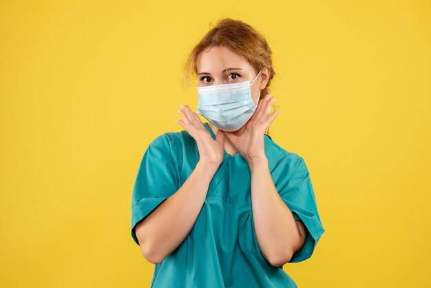 Front view of young female doctor in medical suit and mask on yellow wall