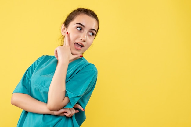 Front view young female doctor in medical suit posing on yellow background