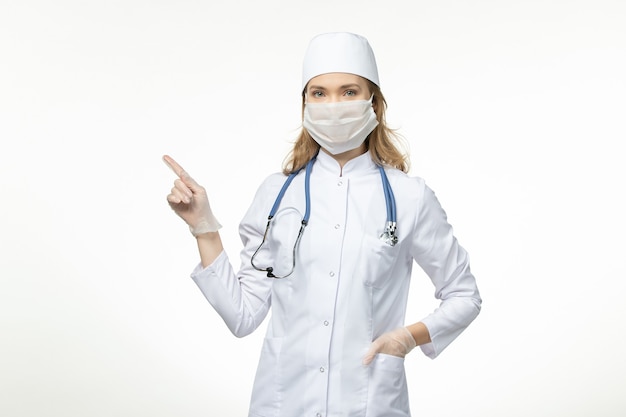 흰색 책상에 코로나 바이러스로 인해 보호 마스크를 착용하는 의료 소송에서 전면보기 젊은 여성 의사