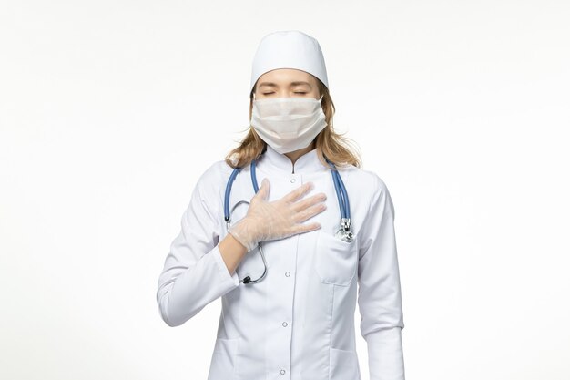 Front view young female doctor in medical suit wearing protective mask due to coronavirus on white floor