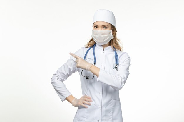 白い表面のコロナウイルスによる保護マスクを身に着けている医療スーツの若い女性医師の正面図