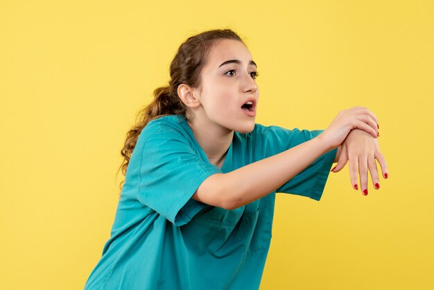 Front view young female doctor in medical suit with hurt hand on yellow background