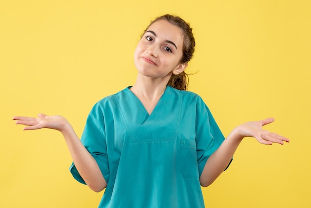 Vista frontale giovane medico femminile in tuta medica su sfondo giallo virus pandemia salute emozione ospedale di colore