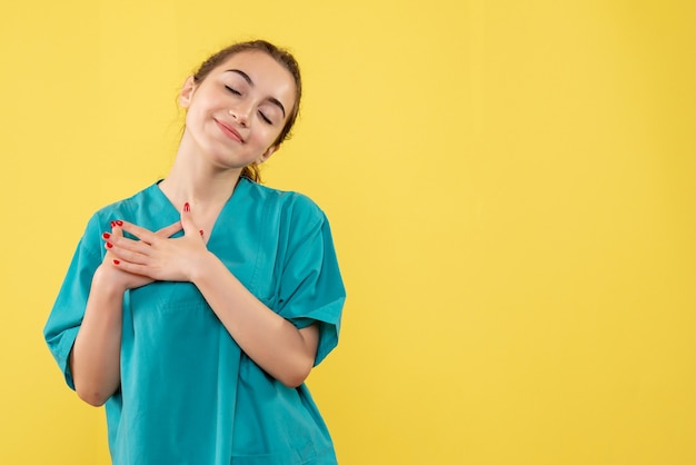 Front view of young female doctor in medical suit on a yellow wall