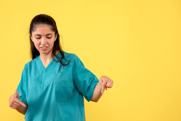 Front view of young female doctor pointing at wall. on yellow wall