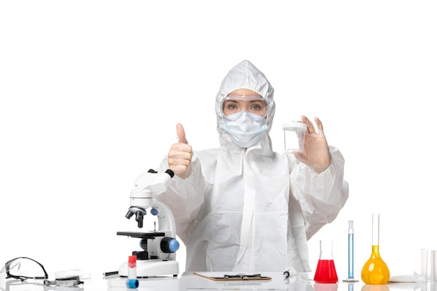 Front view young female doctor in protective suit with mask due to covid holding empty flask on white background splash pandemic covid- virus