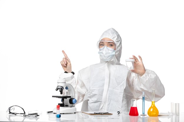 Front view young female doctor in protective suit with mask due to covid holding flask on light-white background splash pandemic covid virus