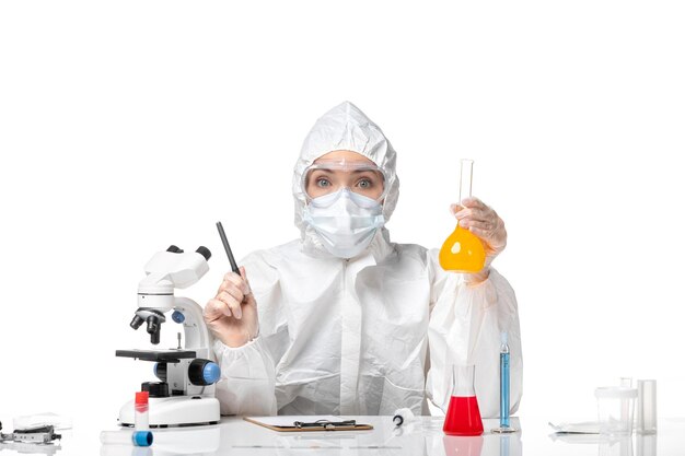 Front view young female doctor in protective suit with mask due to covid holding yellow solution on a light white background splash pandemic covid- virus