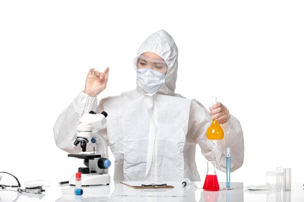 Вид спереди молодая женщина-врач в защитном костюме с маской из-за covid, держащего желтый раствор на белом фоне, всплеск пандемического вируса covid