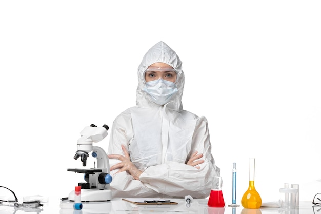 Front view young female doctor in protective suit with mask due to covid sitting on light white background pandemic splash covid- virus