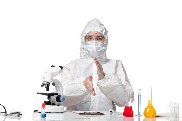 Front view young female doctor in protective suit with mask due to covid sitting and smiling on white background virus pandemic splash covid-