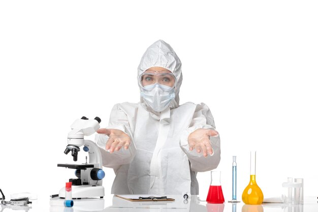 白い背景のウイルスパンデミックスプラッシュcovid-に座っているcovidのためにマスク付きの防護服を着た若い女性医師の正面図