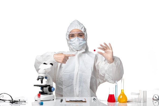 Вид спереди молодая женщина-врач в защитном костюме с маской из-за covid, работающего на белом столе, здоровье пандемического вируса covid