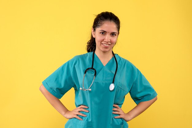黄色の壁に腰に手を置く若い女性医師の正面図