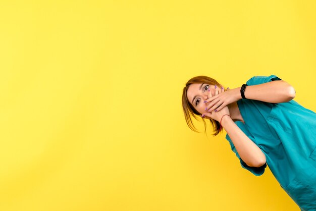 Front view of young female doctor shocked on yellow wall