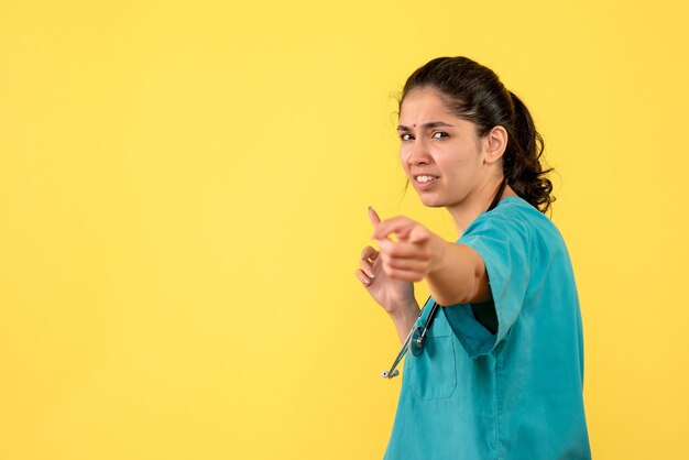 Front view of young female doctor standing on yellow wall