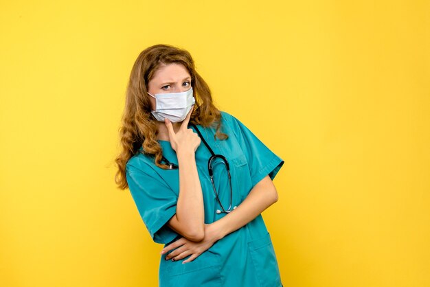 Вид спереди молодая женщина-врач думает в маске на желтом пространстве