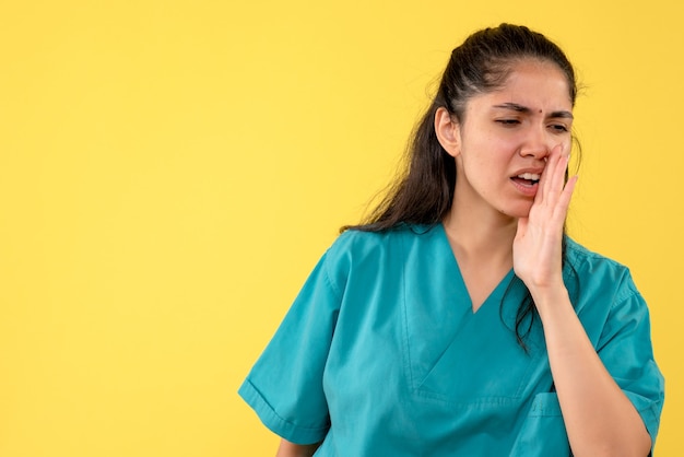 Front view of young female doctor in uniform calling someone on yellow wall