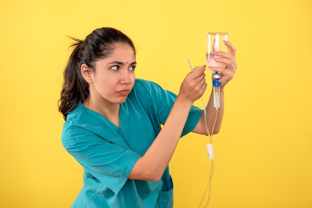 Front view of young female doctor using serum on yellow wall