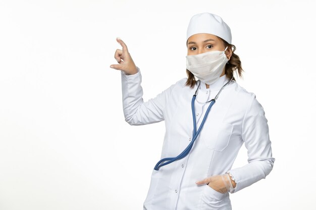밝은 흰색 표면에 코로나 바이러스로 인해 보호 멸균 마스크를 착용하는 전면보기 젊은 여성 의사