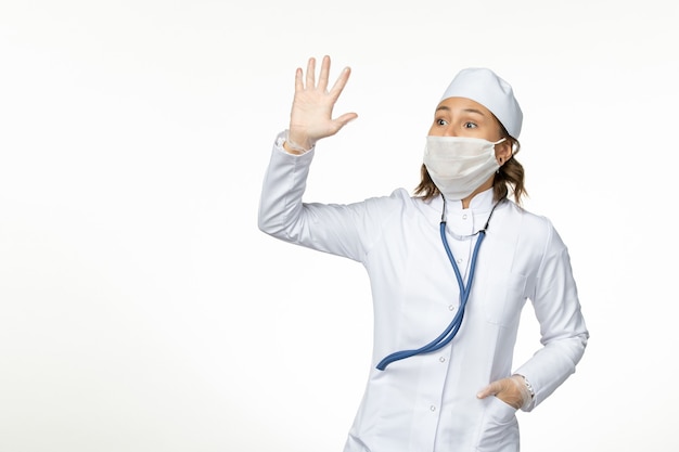 흰색 표면에 물결 치는 코로나 바이러스로 인해 보호 멸균 마스크를 착용하는 전면보기 젊은 여성 의사