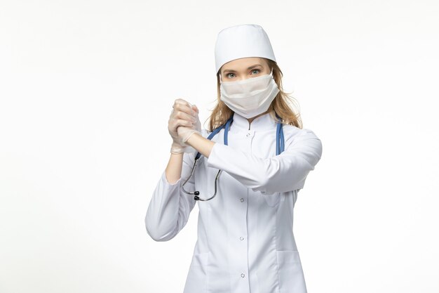 Front view young female doctor wearing protective sterile mask due to coronavirus on white desk