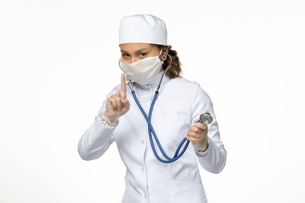 Front view young female doctor wearing protective sterile mask due to coronavirus on the white surface