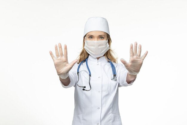 Front view young female doctor wearing protective sterile mask due to coronavirus on the white surface