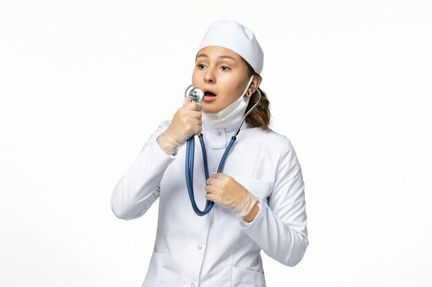 흰색 표면에 코로나 바이러스로 인해 보호 멸균 마스크를 착용하는 전면보기 젊은 여성 의사